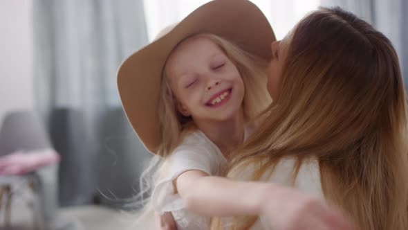 Adorable Little Girl in Wide Brim Hat Hugging Mother at Home