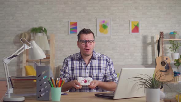 Young Man in Glasses Sits at a Laptop and Coughs with Blood