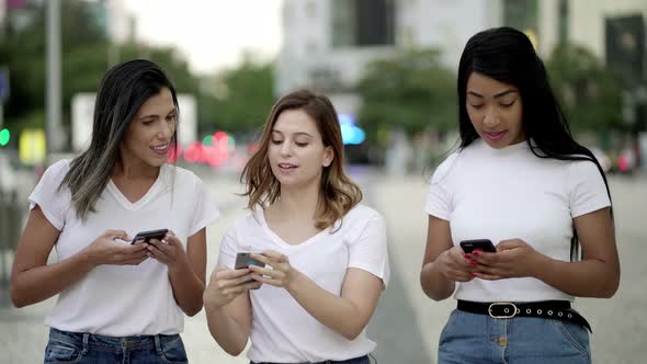 Joyful Friends Walking on Street and Texting on Smartphones