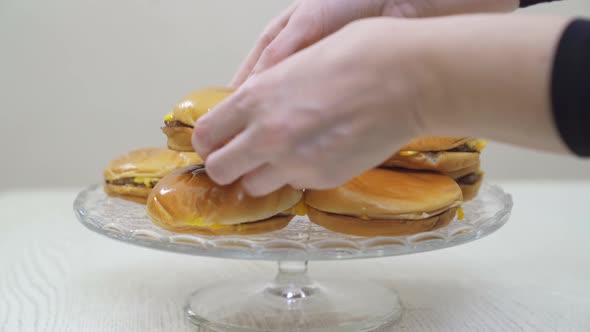 Hands Place Cheeseburgers on a Round Glass Dish