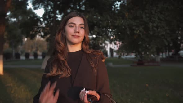 Portrait of a Beautiful Young Girl in Black Stylish Clothes Standing Among the Trees on a City