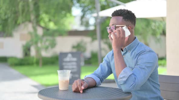 African Man Talking on Smartphone in Outdoor Cafe