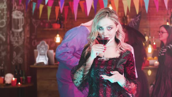 Young Woman Dressed in a Vampire Costume Drinks Blood at a Halloween Party