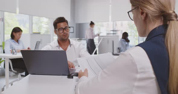 View Over Shoulder of Female Executive Collaborating with Indian Employee Sitting at Desk in Office