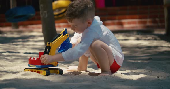 Child Plays with a Plastic Car in the Sand on the Beach