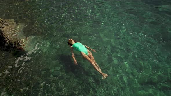 Slow Motion Top View of Sexy Stunning Woman in Green Swimsuit Floating on Back and Relaxing in Clear