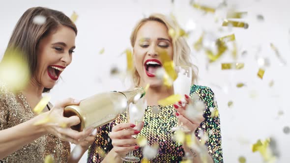 Female friends drinking champagne and dancing among confetti