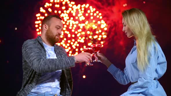 Happy Couple Loving Knocking Glasses Wine on Background Firework in Night Date.