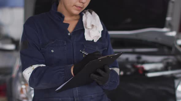 Portrait of female mechanic taking notes on clipboard and smiling at a car service station