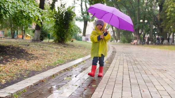 Slow Motion Video of Cute Little Boy in Raincoat and Rubber Boots Holding Umbrella and Walking in