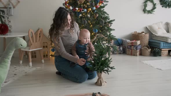 Mother Playing with Cute Baby Near Christmas Tree