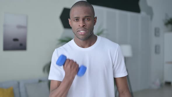 Athletic African Man Working Out with Dumbbells at Home
