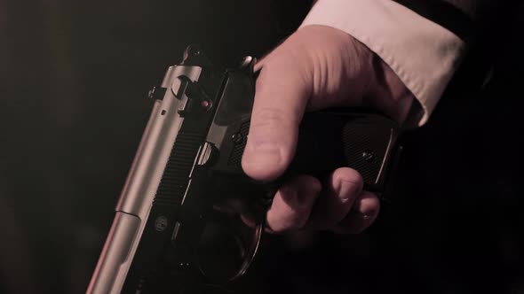 Close up on mafia man in suit's hands holding a pistol. Dark background