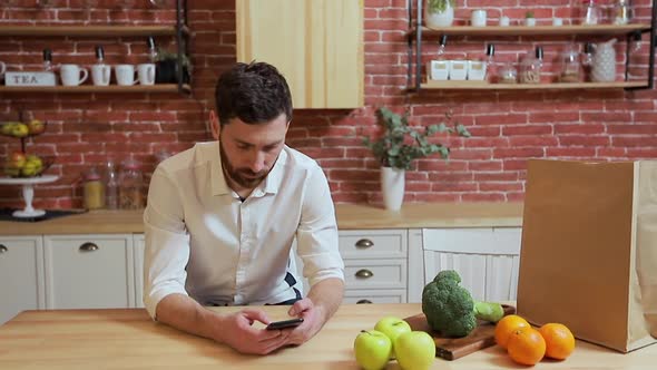 Man Browsing on Mobile Phone at Home Kitchen. Handsome Young Man Browsing on Smartphone Smiling