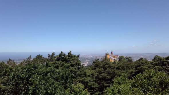 Overlooking colorful Pena Palace in Portugal rising above trees on windy clear day.