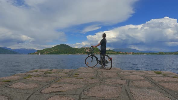 Back view of solitary woman holding bicycle on concrete jetty edge of Maggiore lake in Italy