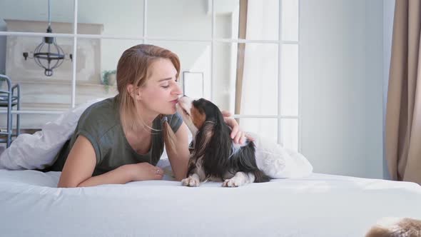 A Woman of European Appearance Lies on a Bed in a Cozy Bedroom with Her Beloved Dog and Show
