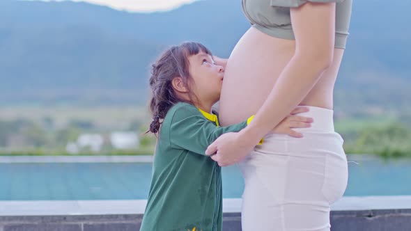 Adorable kid girl hugging and kissing pregnant mother belly