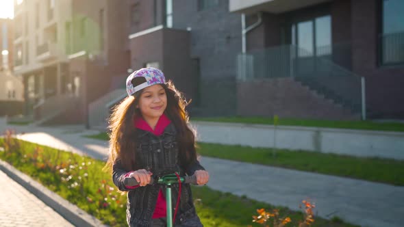 Brunette Girl Riding a Scooter at Sunset in Her Area.