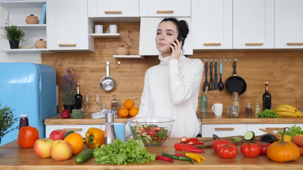 Young Woman Talking On Smartphone At Home While Cooking In Kitchen.