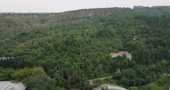 Dolly out aerial shot of the Tbilisi forest, revealing the Kartlis Deda statue.