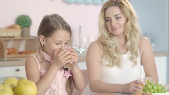 Beautiful Little Girl Drinking Orange Juice and Showing Thumb Up As Smiling Woman Admiring Daughter