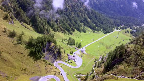 Winding road along Dolomite mountain pass in the Italian Alps with a water stream and lodge along th