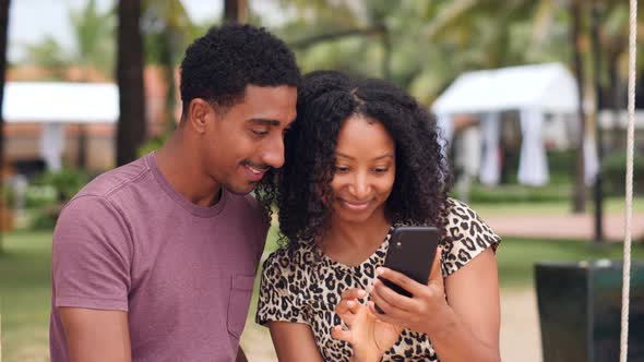 Carefree African Young Couple Watching at a Smartphone Smiling and Laughing