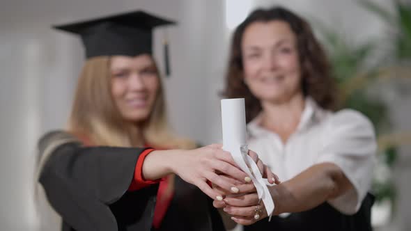 Closeup Rolled Graduation Diploma with Ribbon in Hands of Happy Caucasian Mother and Daughter