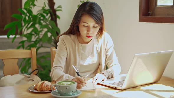 Young woman with cup of coffee sitting and working on laptop at coffee shop