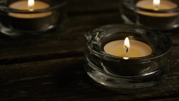 Tea candles with flaming wicks on a wooden background