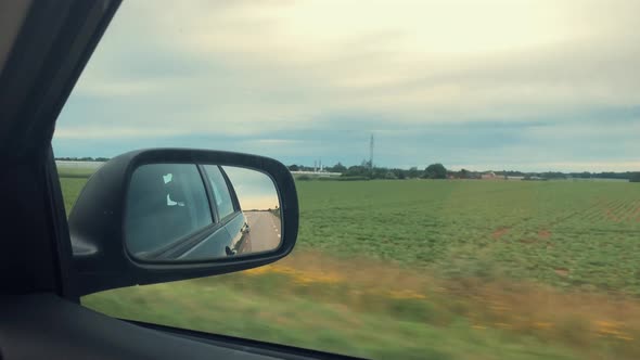 Car mirror view of green fields