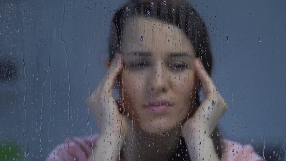 Woman Suffering Migraine, Rubbing Temples Near Rainy Window, Weather Sensitivity