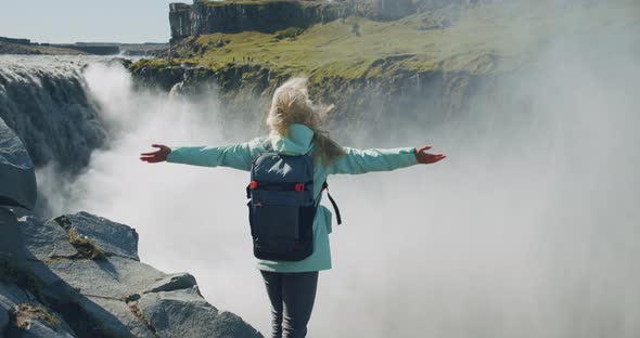 Woman Standing on the Edge of the Cliff and Raising Her Hands Up in the Air Wiht Beautiful Detifoss