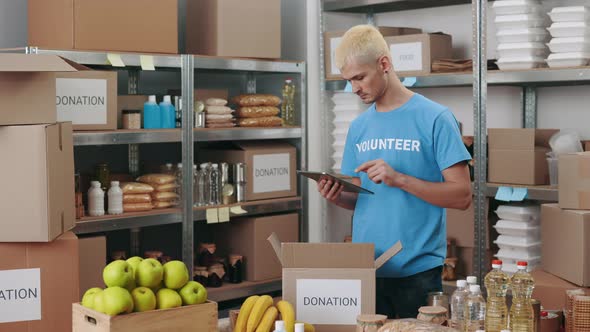 Focused Male Volunteer Using Tablet for Packing Donation Box