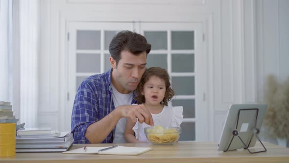 Family young father eating potato chips in mouth with little daughter together and watch cartoons 