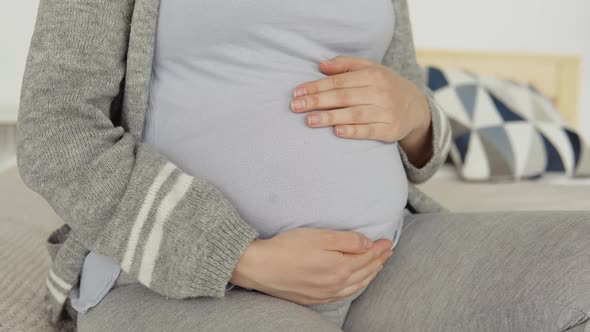 Close Up of Pregnant Woman in Home Clothes Sitting on a Double Bed