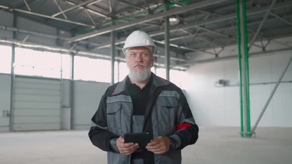 Handheld Adult Man Technical Engineer Walks on a Warehouse and Uses a Screen Tablet Perform a