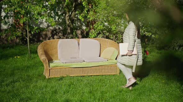 Comfortable Couch in Sunny Spring Garden with Confident Asian Woman Entering Sitting Down Opening