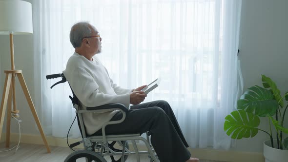 Asian senior male sit alone on wheelchair and looks family photographs missing his relative and wife