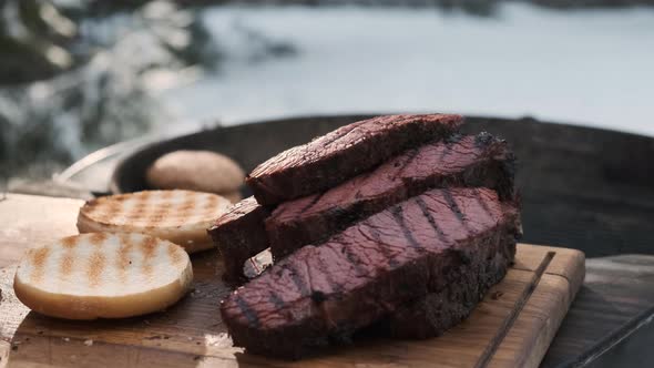 Delicious Juicy Steak Freshly Removed From Grill Lies on Cutting Board Next to Burger Buns