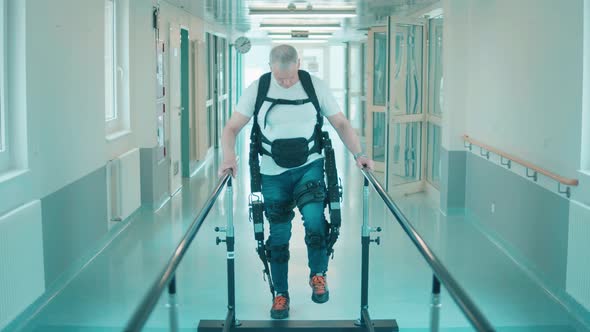 Disabled Man in the Exoskeleton is Slowly Walking Along the Hospital