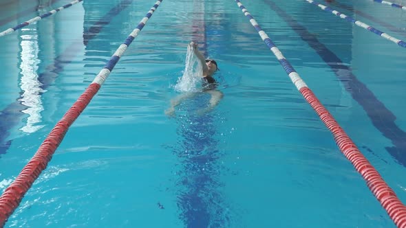 Young Girl in Goggles and Cap Swimming Back Crawl Stroke Style in the Blue Water Pool