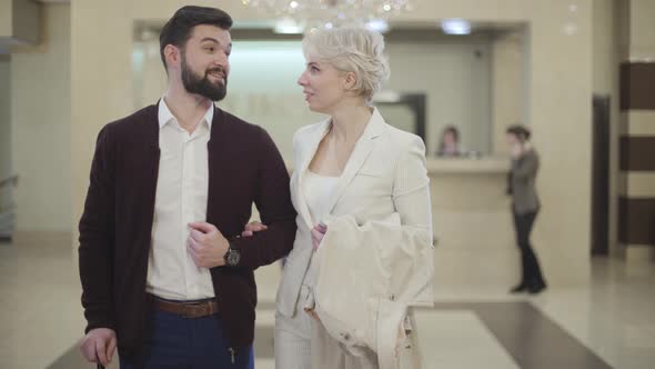 Beautiful Young Caucasian Couple Talking and Looking at Camera in Luxurious Hotel Lobby