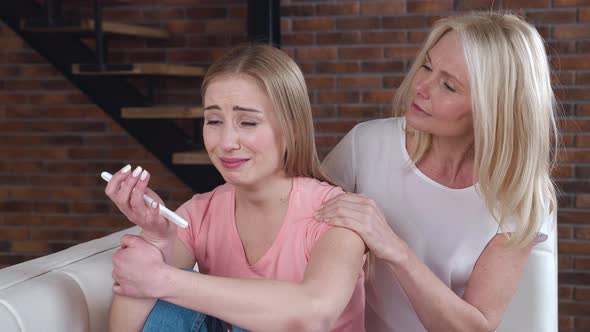 Young Adult Woman is Suffering and Crying From an Unwanted Pregnancy Holding a Pregnancy Test in Her