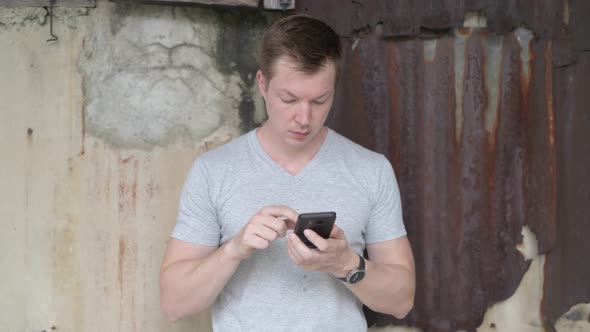 Young Happy Tourist Man Smiling While Using Phone Against Grungy Wall