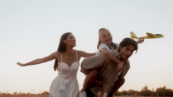 Happy Young Parents And Teen Daughter Having Fun Outdoors Playing With Plane Toy