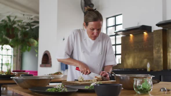 Caucasian female chef preparing a dish and smiling in a kitchen