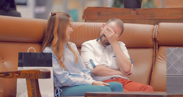 Man and a Girl are Sitting on a Sofa in a Mall Talking and Laughing