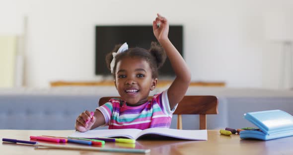 Happy african american girl raising hand during online school at home